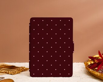 Puede incluir: Una funda tipo folio burdeos con un patrón repetido de pequeños lunares rosa claro. La funda tiene un cierre magnético en el lado derecho. El fondo es de color neutro.