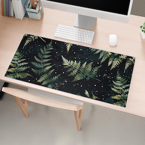 May include: A black and green desk mat with a fern pattern. The mat is on a light wood desk with a computer, keyboard, and mouse.