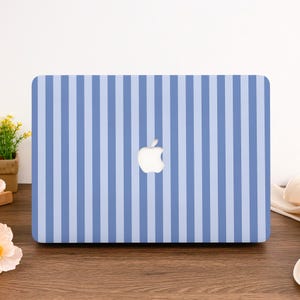 Può includere: Custodia per laptop a righe blu e bianche con il logo Apple al centro. La custodia presenta un motivo a righe verticali in blu chiaro e medio. La custodia per laptop è su una superficie di legno.