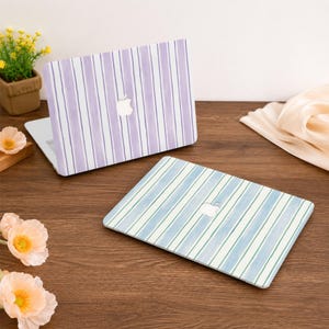 May include: Two laptop cases with striped designs. One case features vertical stripes in shades of purple and white. The other case has blue and green stripes. Both cases have a white apple logo cutout.
