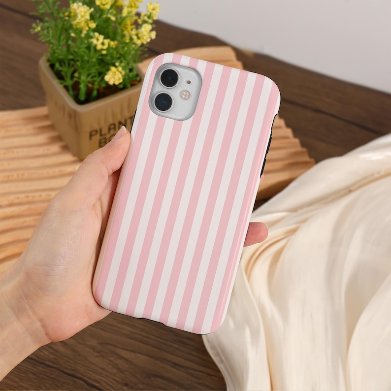 May include: A pink and white striped phone case for an iPhone. The case has a cutout for the camera lens.