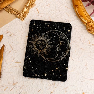 Pode incluir: Uma capa preta para leitor de e-books com um design dourado de um sol e uma lua com estrelas em um fundo preto.