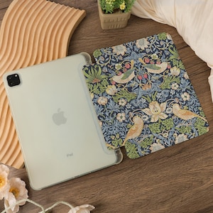 May include: An iPad in a clear case next to a patterned cover. The cover features a dark blue background with a floral and bird design in green, white, and yellow. The iPad is light green.