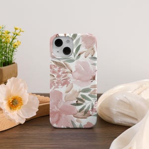 Könnte beinhalten: Eine Handyhülle mit floralem Muster aus rosa und braunen Blumen und grünen Blättern auf weißem Hintergrund. Die Hülle hat eine glänzende Oberfläche und einen Kameraausschnitt.