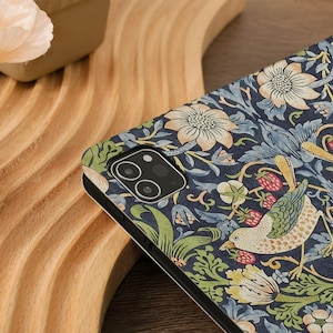 May include: A phone case with a floral and bird pattern. The case features a dark blue background with cream-colored flowers, green leaves, and a bird design. The case has a black border and a camera cutout.