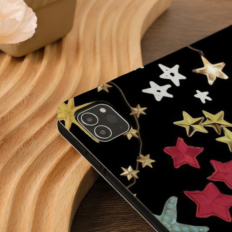 Pu&ograve; includere: Una custodia per telefono nera con un design di stelle dorate e bianche su sfondo nero. La custodia ha un ritaglio per l'obiettivo della fotocamera.