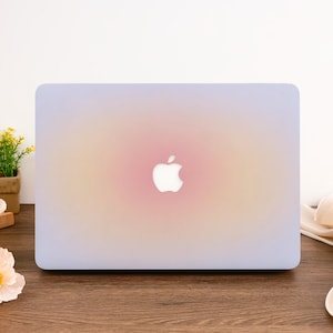 Puede incluir: Un portátil de color lila claro con un degradado de rosa y amarillo. El portátil tiene un logotipo de Apple blanco en la tapa.