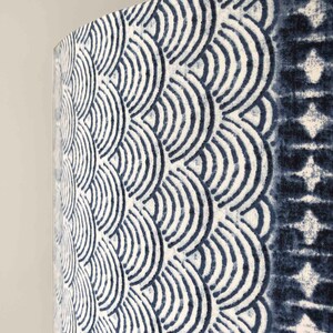 May include: A close-up of a white fabric lampshade with a blue and white geometric pattern. The pattern is made up of repeating arcs that resemble waves.