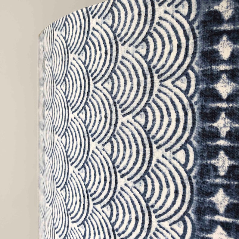 May include: A close-up of a white fabric lampshade with a blue and white geometric pattern. The pattern is made up of repeating arcs that resemble waves.