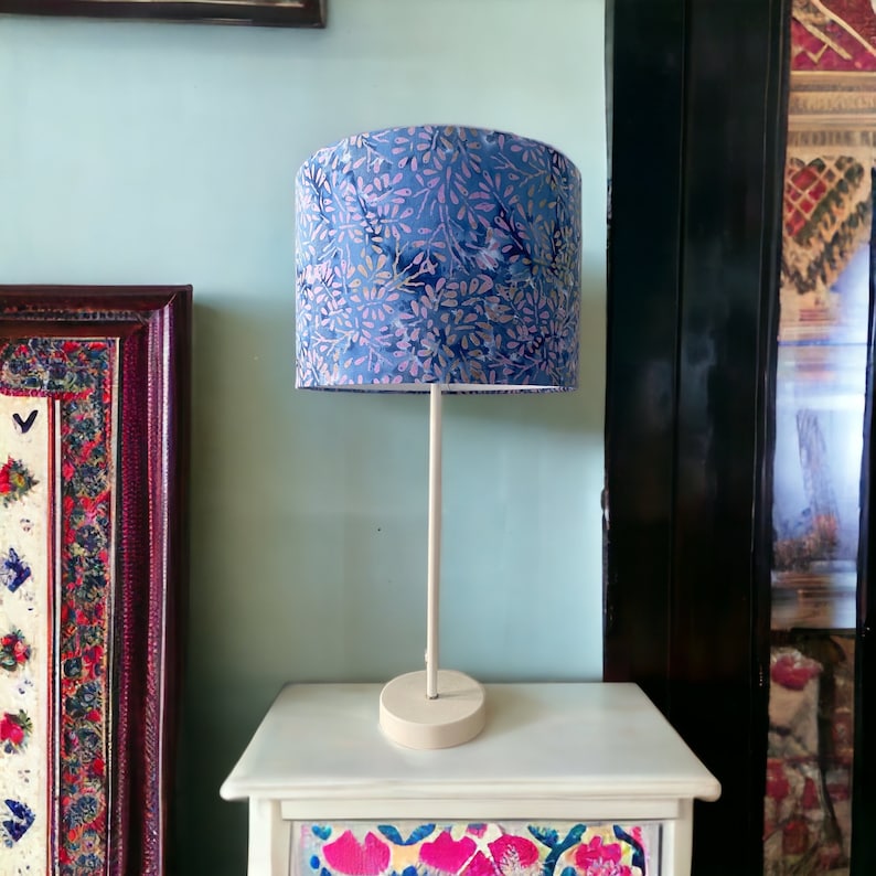 Pu&ograve; includere: Una lampada da tavolo bianca con un paralume a motivi floreali blu e rosa. La lampada &egrave; su un comodino bianco con un cassetto a motivi floreali.