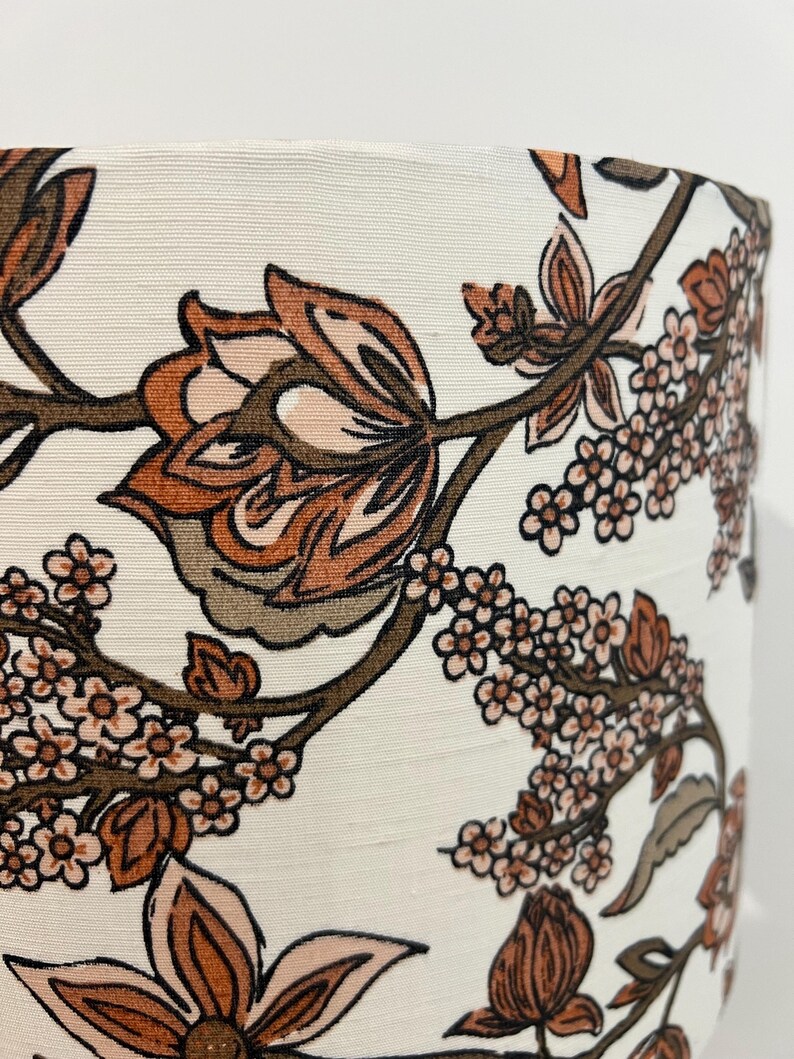 May include: A white lampshade with a floral pattern in shades of brown and pink. The pattern features large flowers and smaller blossoms.