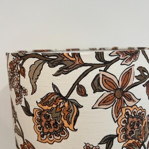 May include: A white lampshade with a floral pattern in shades of brown, orange, and pink. The flowers are stylized and have a paisley-like design.