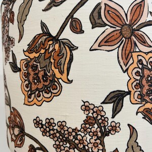 May include: A white lampshade with a floral pattern in shades of brown, orange, and pink. The flowers are stylized and have a vintage feel.