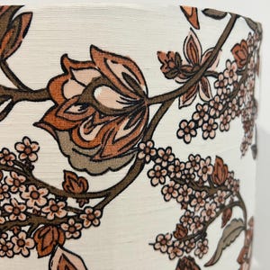 May include: A white lampshade with a floral pattern in shades of brown and pink. The pattern features large flowers and smaller blossoms.