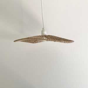 May include: A woven, light brown, lampshade with a white cord hanging from the ceiling.