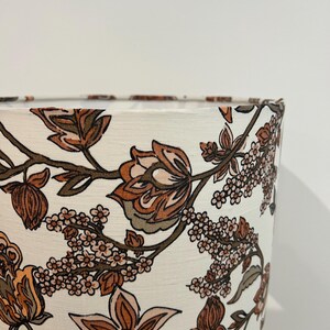 May include: A white lampshade with a floral pattern in shades of brown, pink, and green. The pattern features stylized flowers and leaves.