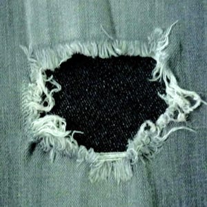 Peut inclure: Un gros plan sur une paire de jeans bleus avec un grand trou effiloché dans le tissu.