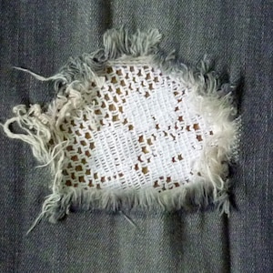 May include: A close-up of a pair of blue jeans with a hole that has been patched with white crochet fabric.