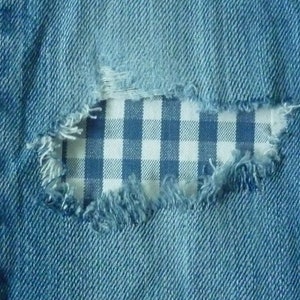 May include: A close-up of blue denim fabric with a hole revealing a white and blue gingham pattern underneath.