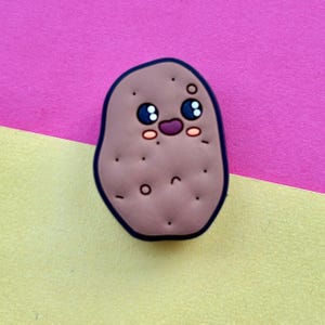 May include: A brown potato with a cute cartoon face, smiling with big eyes and rosy cheeks. The potato is on a yellow and pink background.