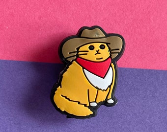 Peut inclure: Un chat de dessin animé jaune portant un chapeau de cowboy marron et un bandana rouge avec une bordure blanche. Le chat est assis les jambes croisées et a une expression amicale.