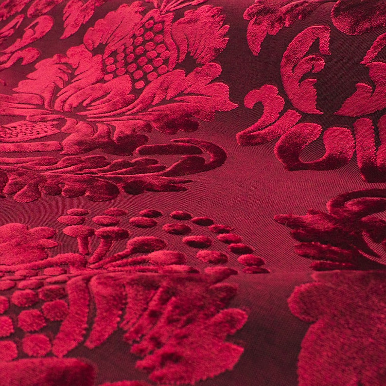 May include: Close-up of a deep red velvet fabric with a raised, embossed floral pattern.