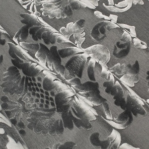 May include: Close-up of a gray fabric with a raised, embossed floral pattern. The fabric has a soft, velvety texture.
