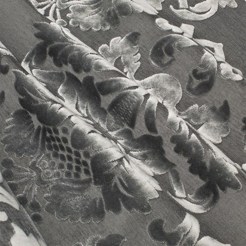 May include: Close-up of a gray fabric with a raised, embossed floral pattern. The fabric has a soft, velvety texture.