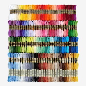 Può includere: Una collezione di 100 rocchetti di filo da ricamo in un arcobaleno di colori, disposti in file. Ogni rocchetto ha un'etichetta dorata con testo nero.