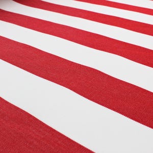 May include: Close-up of a fabric with bold, diagonal red and white stripes. The stripes are evenly spaced and create a visually striking pattern. The fabric appears to be a medium weight material, suitable for various projects.