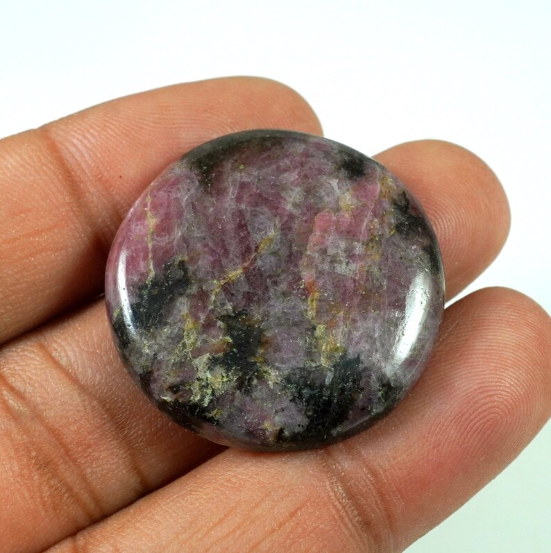 May include: A round, polished cabochon of pink and black rhodochrosite. The stone has a swirling pattern of pink and black.