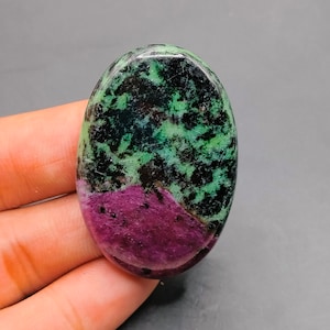 May include: Oval-shaped green and purple gemstone with black and white markings. The gemstone is smooth and polished.