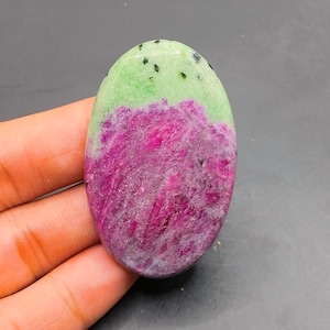 May include: Oval-shaped green and pink gemstone cabochon with black flecks.
