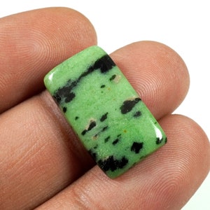May include: A green and black gemstone cabochon with a rectangular shape. The stone has a mottled pattern of black and green.
