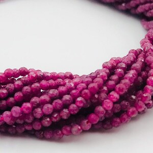 Puede incluir: Una hebra de cuentas facetadas de color rojo rubí. Las cuentas son pequeñas y redondas, y están enhebradas en un hilo transparente.