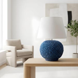 Puede incluir: Lámpara de mesa azul marino con base esférica texturizada y pantalla blanca. La lámpara está sobre una mesa de madera clara. La base tiene un patrón de pequeñas formas en relieve.