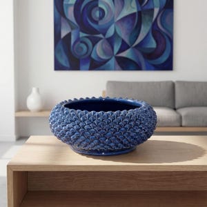 Può includere: Una ciotola rotonda in ceramica blu navy con un motivo strutturato a scaglie all'esterno. La ciotola è su un tavolo di legno chiaro. Un dipinto con sfumature di blu è appeso sullo sfondo. Il diametro della ciotola è di circa 30 cm.
