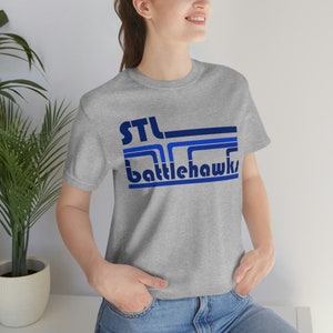 May include: A gray t-shirt with a blue and navy blue graphic print that says "STL Battlehawks".