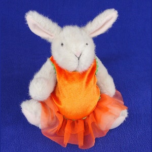 Puede incluir: Conejo de peluche blanco con un vestido naranja con ribete verde y una falda de tul.