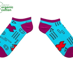 May include: A pair of turquoise blue ankle socks with a geometric pattern in black, red, and white. The socks have a purple cuff and the text "decoosh" is printed on the socks.