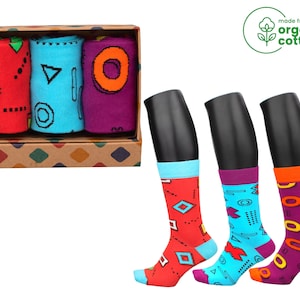 May include: A set of three pairs of colorful socks in a brown box. The socks feature geometric patterns in red, blue, and purple. The box has the text "made from organic cotton" on a green tag.