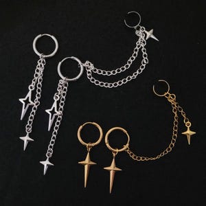 May include: An assortment of silver and gold-toned earrings. The silver earrings feature star charms and chain details. The gold earrings have star pendants and chain accents. The earrings are displayed on a black background.