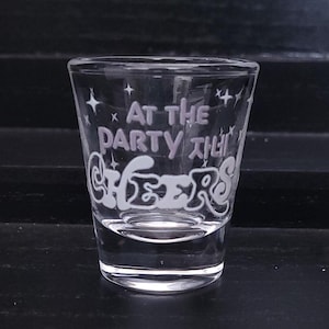 Könnte beinhalten: Ein klares Glas-Schnapsglas mit dem Text "At the party then Cheers" in weiß mit rosa Akzenten und kleinen Sternen.