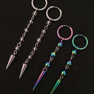 May include: Four earrings with a dangling design. Two earrings have silver hoops, clear beads, and silver cone pendants. The other two earrings have rainbow-colored hoops, iridescent beads, and rainbow cone pendants. The earrings are on a black background.