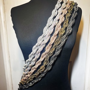 May include: A set of five braided chains in different metal finishes, including silver, gold, and rose gold. The chains are displayed on a black mannequin.