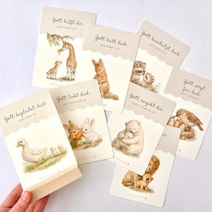 May include: A set of rectangular cards with scalloped top edges, each featuring watercolor illustrations of animal parents and offspring. The cards display German text including Gott hilft dir, Gott h&auml;lt dich, Gott besch&uuml;tzt dich, Gott sorgt f&uuml;r dich, Gott begleitet dich, Gott liebt dich, Gott vergibt dir.