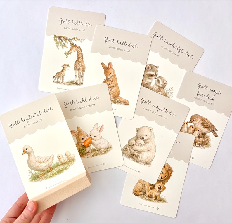 May include: A set of rectangular cards with scalloped top edges, each featuring watercolor illustrations of animal parents and offspring. The cards display German text including Gott hilft dir, Gott h&auml;lt dich, Gott besch&uuml;tzt dich, Gott sorgt f&uuml;r dich, Gott begleitet dich, Gott liebt dich, Gott vergibt dir.