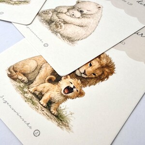 May include: Watercolor illustrations of animals on cards. One card shows a lion and cub, another a polar bear and cub. The cards have a soft, neutral color palette and delicate details, with text in a script font.