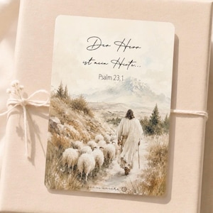 May include: A rectangular card featuring a watercolor illustration of a figure walking with a flock of sheep on a path toward mountains. The text reads: Der Herr ist mein Hirte... Psalm 23,1. The card is tied with white string to a beige box.