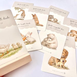 May include: A set of illustrated cards with animal images and German text. The cards feature a duck with ducklings, a giraffe, a rabbit, a bear, a lion, and other animals. The cards are displayed with a wooden holder.